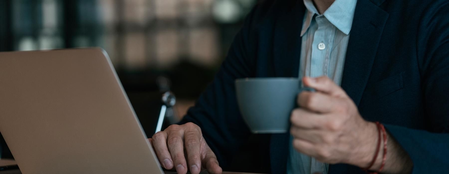 a man holding a cup and looking at a laptop