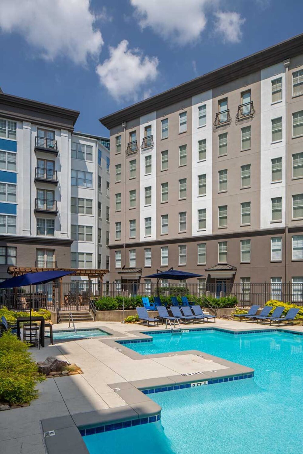 Poolside area with blue side-post umbrella and recliner chairs situated in front of an apartment building